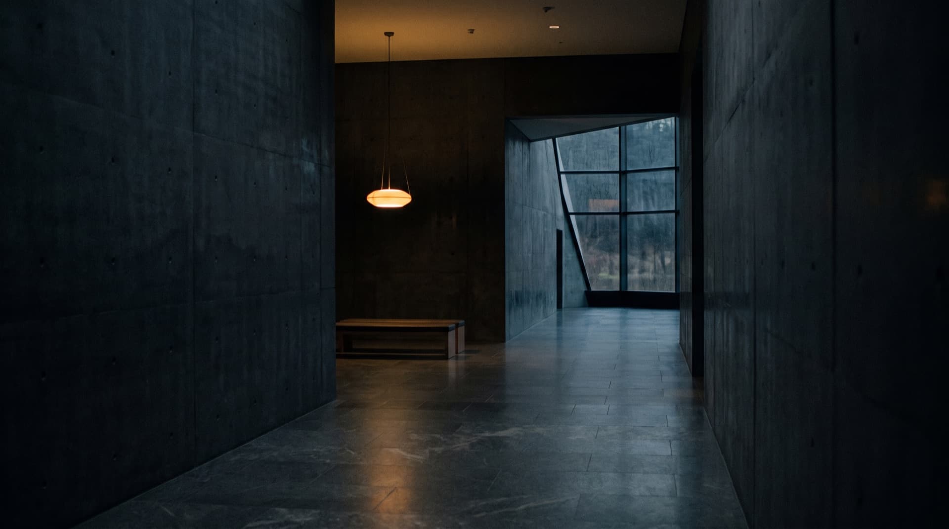 Leeres Foyer aus Sichtbeton bei Nacht, eine Pendelleuchte über einer Sitzbank